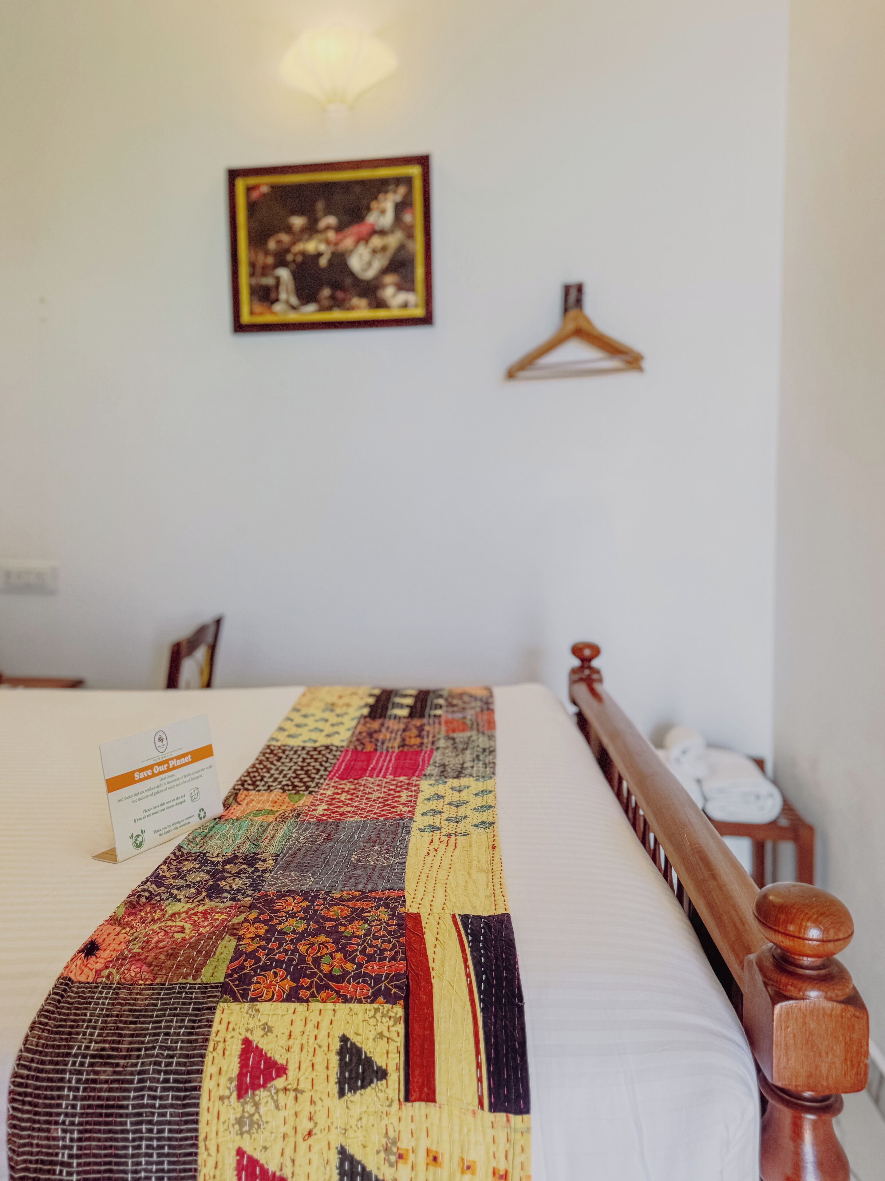 A neatly made bed with a colorful quilt, a framed picture on the wall, and a small wooden chair.