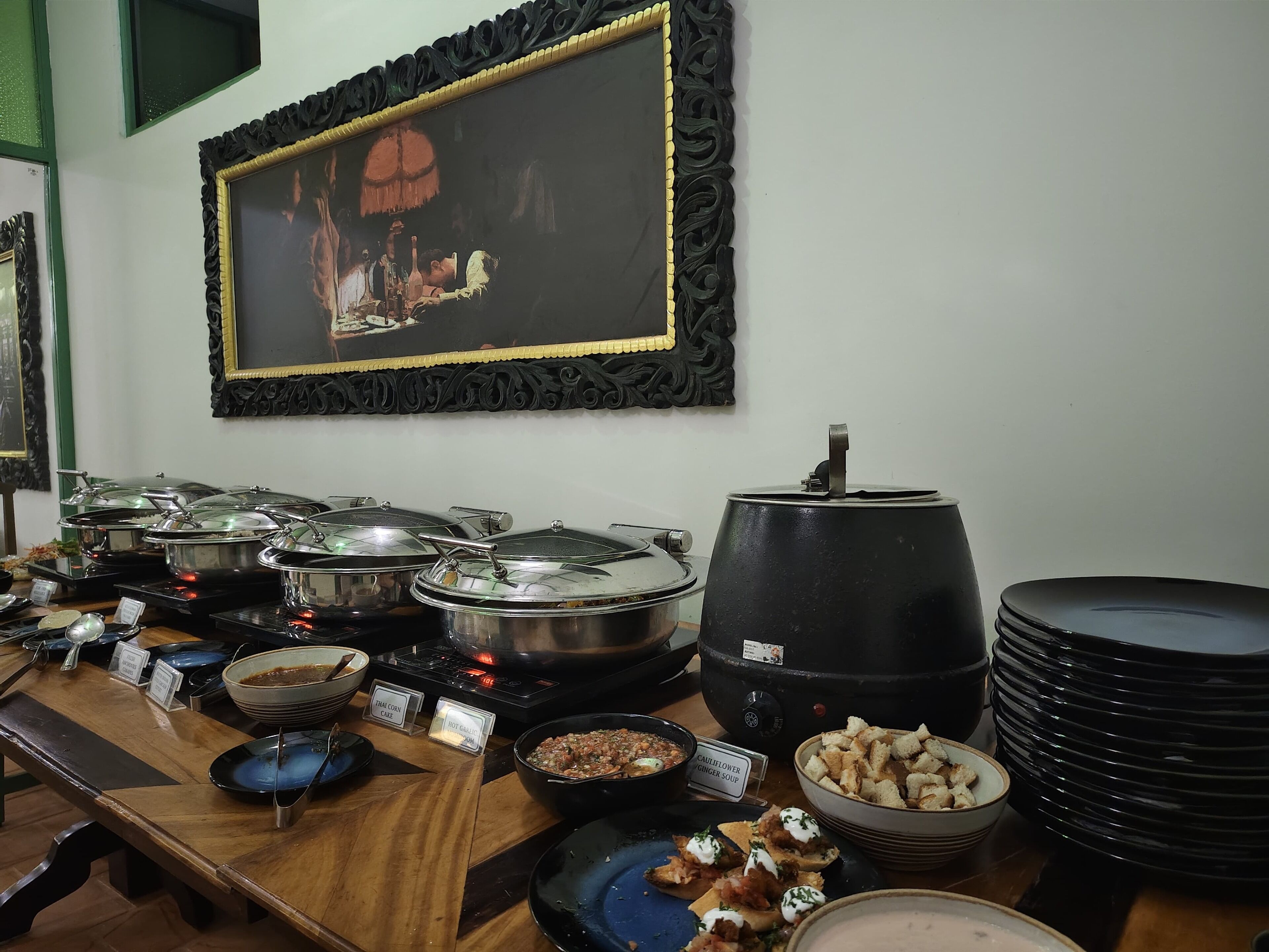 Una mesa de buffet con diversos platos, un cuadro grande enmarco, y un hervidor negro.
