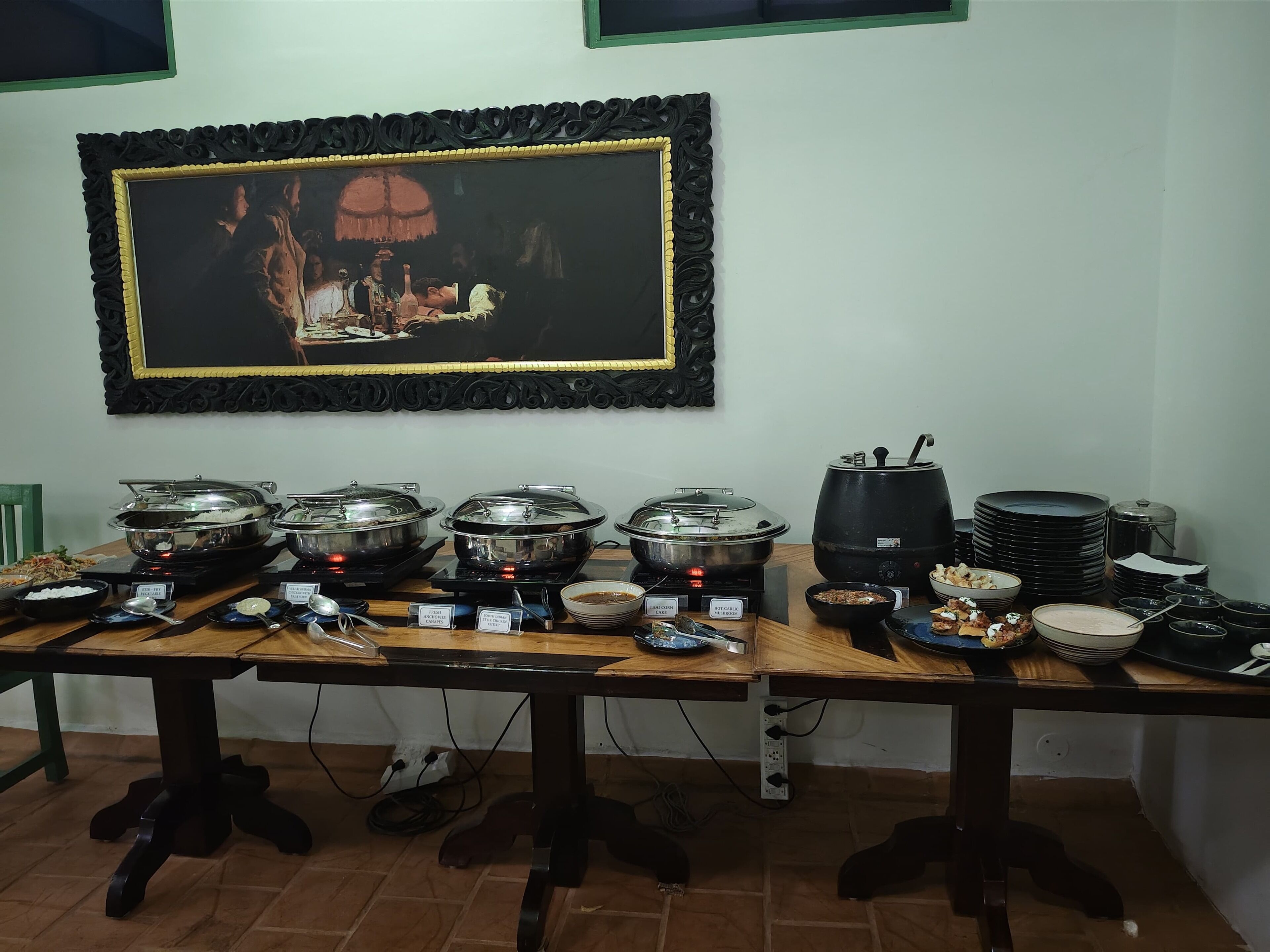 A buffet table with various food items and serving utensils, a framed picture on the wall, and a tiled floor.