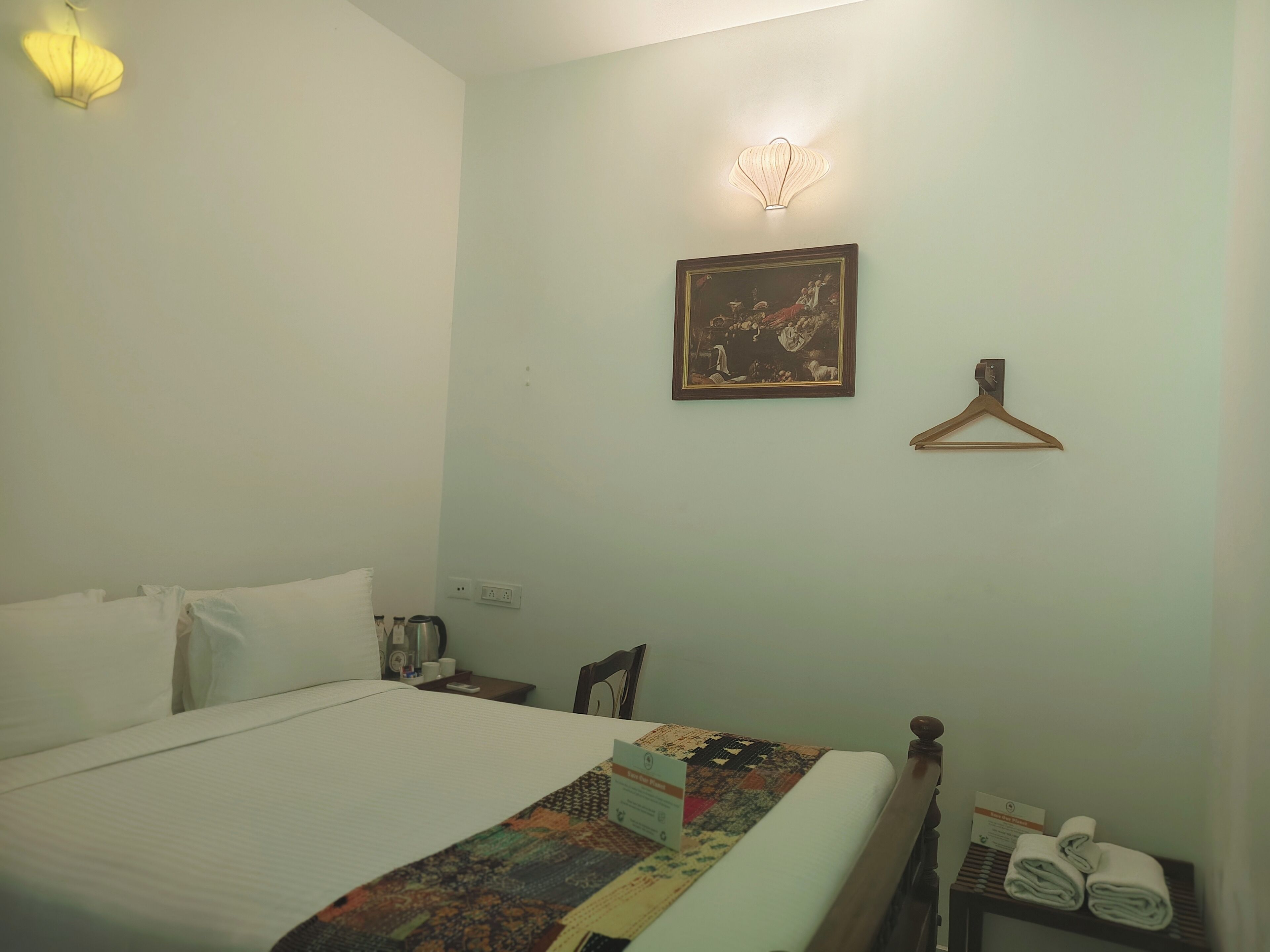 A hotel room with a bed, a nightstand, a lamp, a framed picture, and a coat hanger.