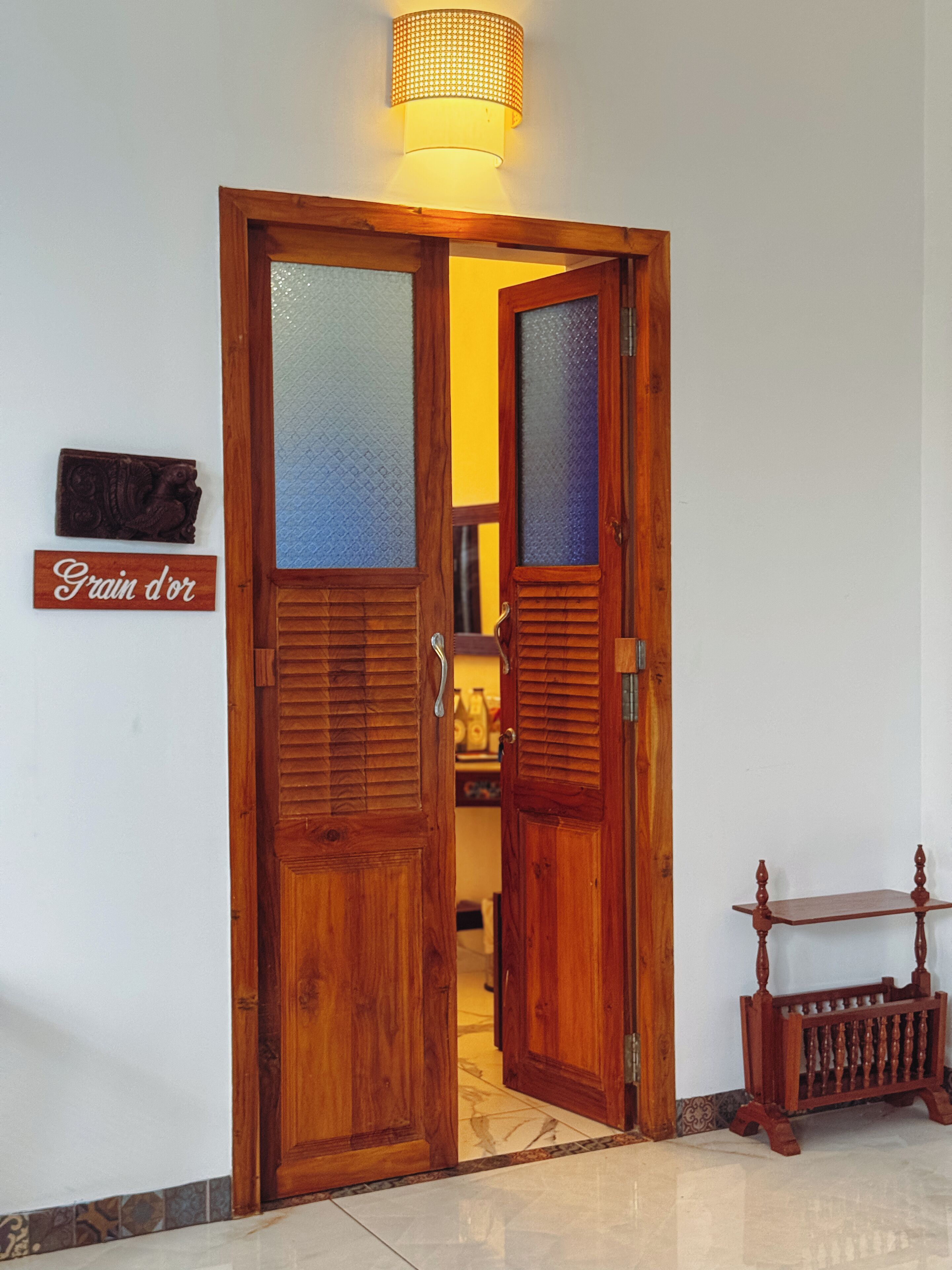 Una puerta de madera con un panel de vidrio esmerilado, un pequeño letrero de madera que dice "Grain d'or" y una pequeña mesa con una superficie decorativa junto a la puerta.