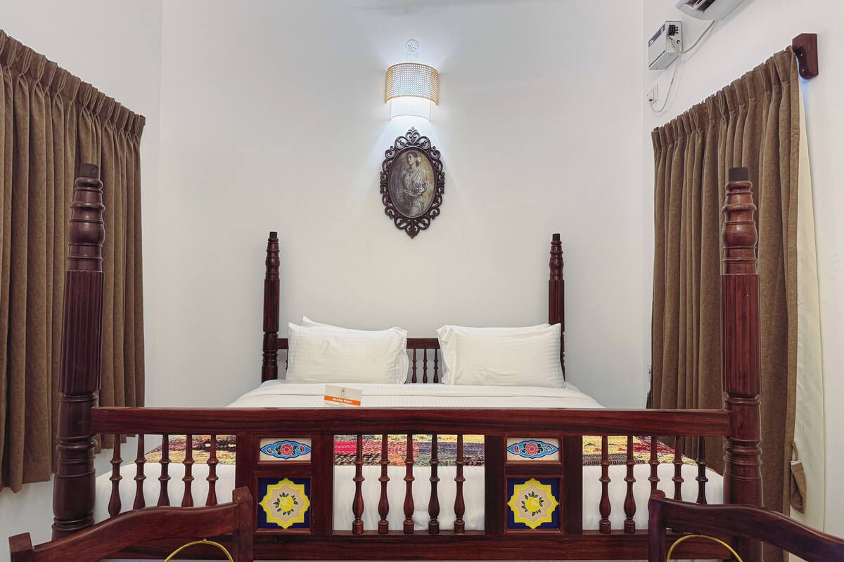 A bedroom with a wooden bed frame, white bedding, and a decorative wall hanging.