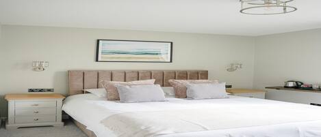 A bedroom with a large bed, two bedside tables, a headboard, a wall-mounted artwork, and a ceiling light fixture.