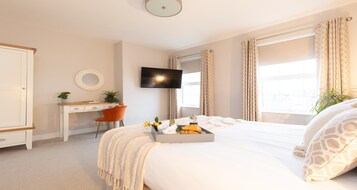 A hotel room with a bed, a desk, a TV, and a window with curtains.