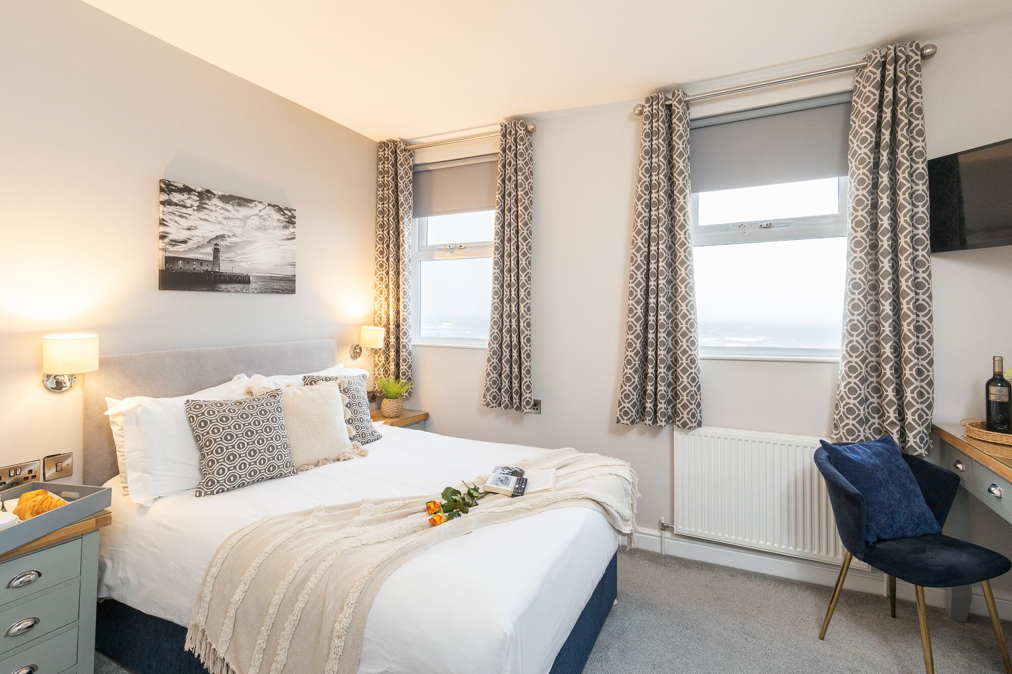 A hotel room with a bed, bedside lamps, a desk with a chair, a TV, and a window with curtains.