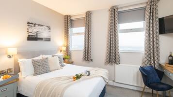A hotel room with a bed, bedside lamps, a desk with a chair, a TV, and a window with curtains.