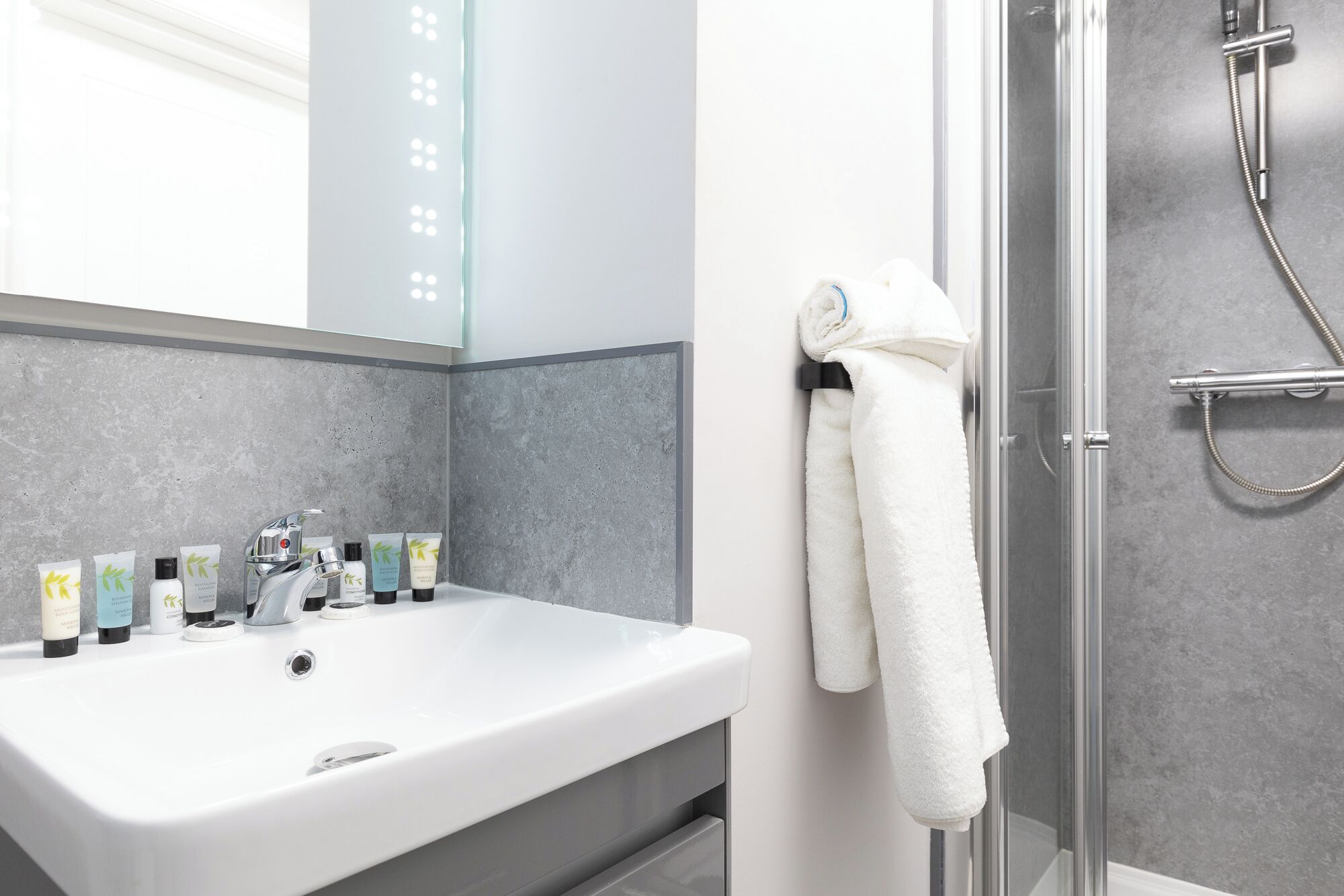 Une salle de bain avec un lavabo blanc, des articles de toilette, un porte-serviettes et une cabine de douche en verre.