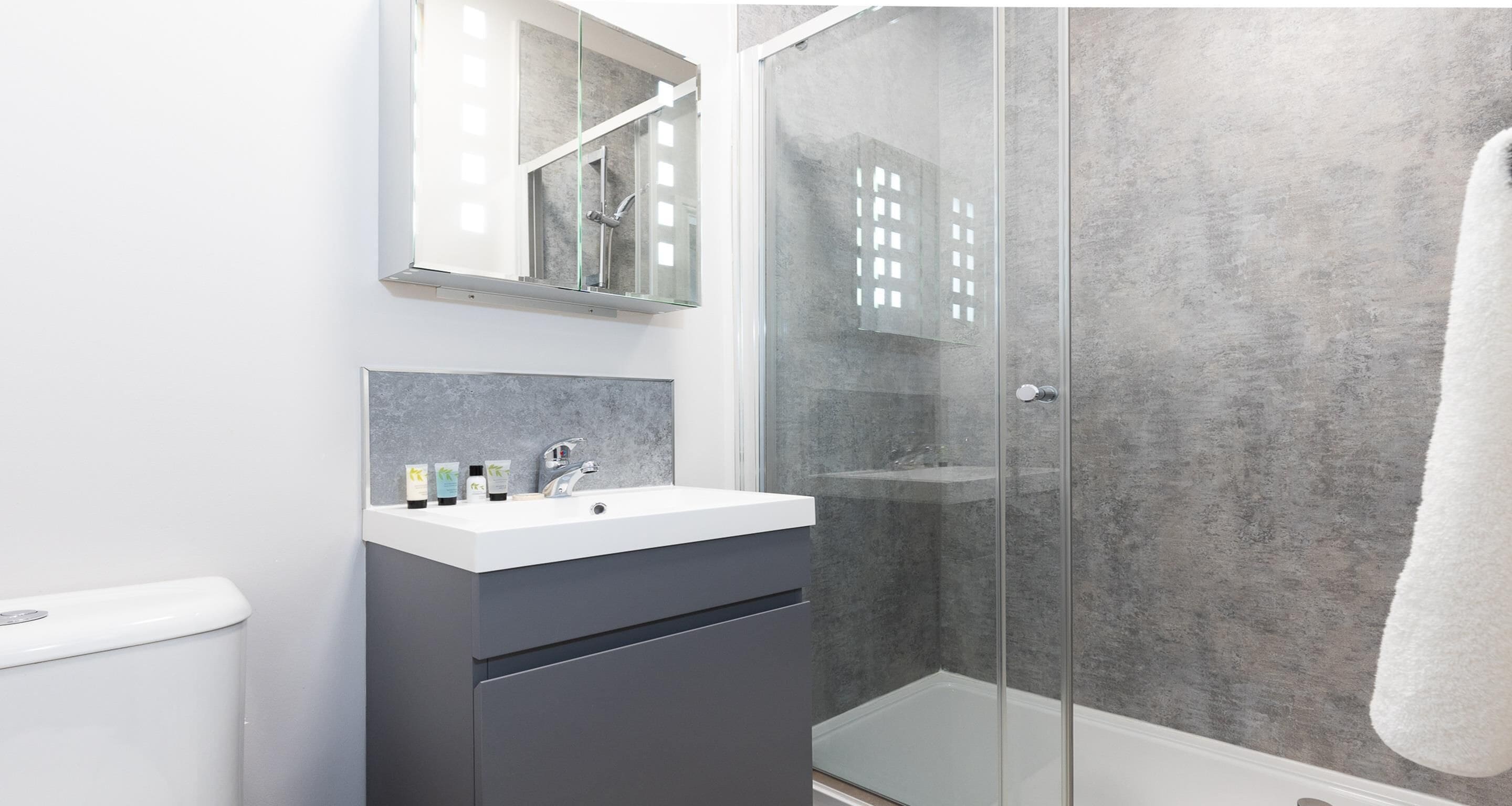 Un baño moderno con ducha envuelta en vidrio, un lavamanos blanco y un espejo sobre él.
