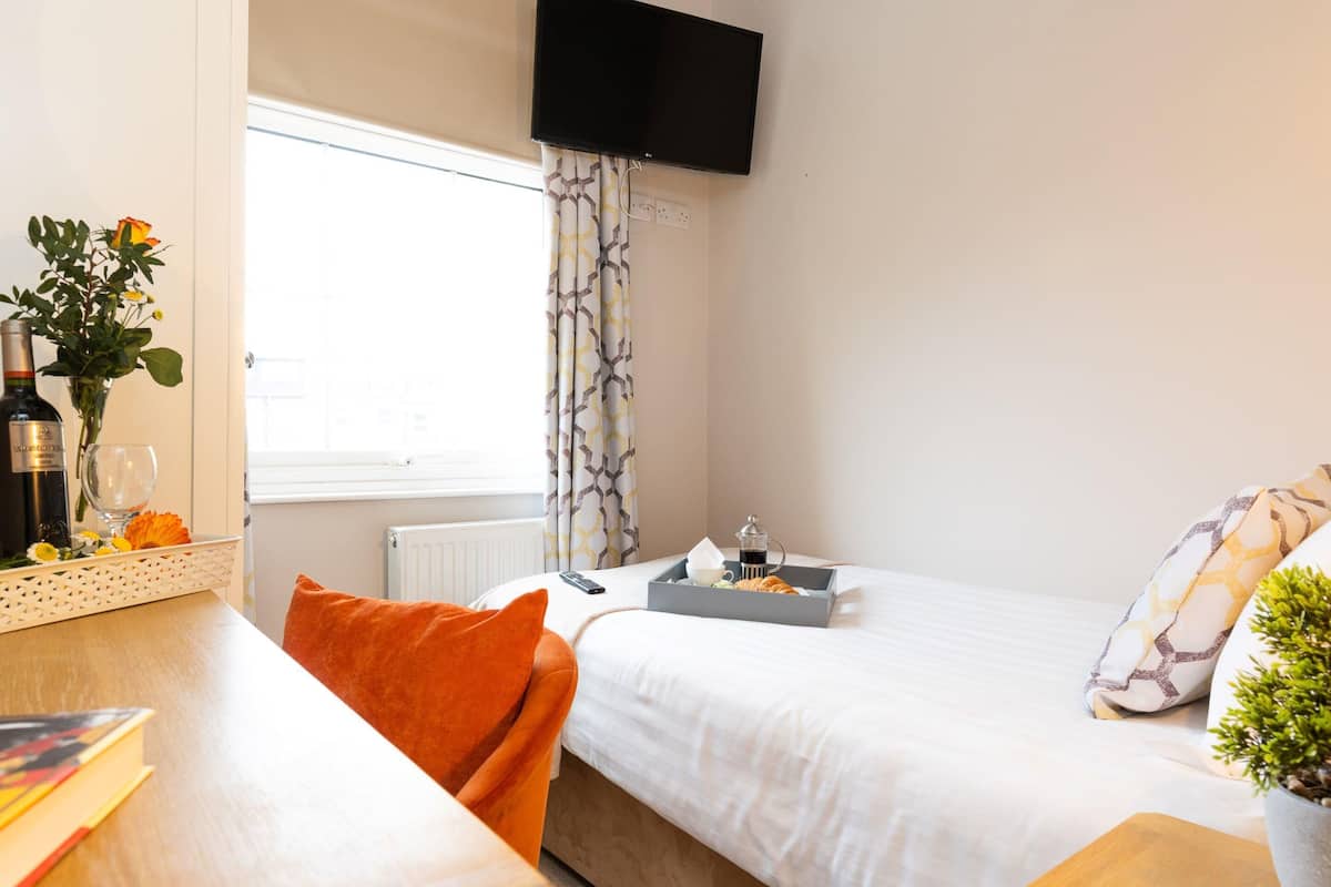 A hotel room with a bed, a bedside table with a tray of breakfast items, a TV mounted on the wall, and a window with curtains.