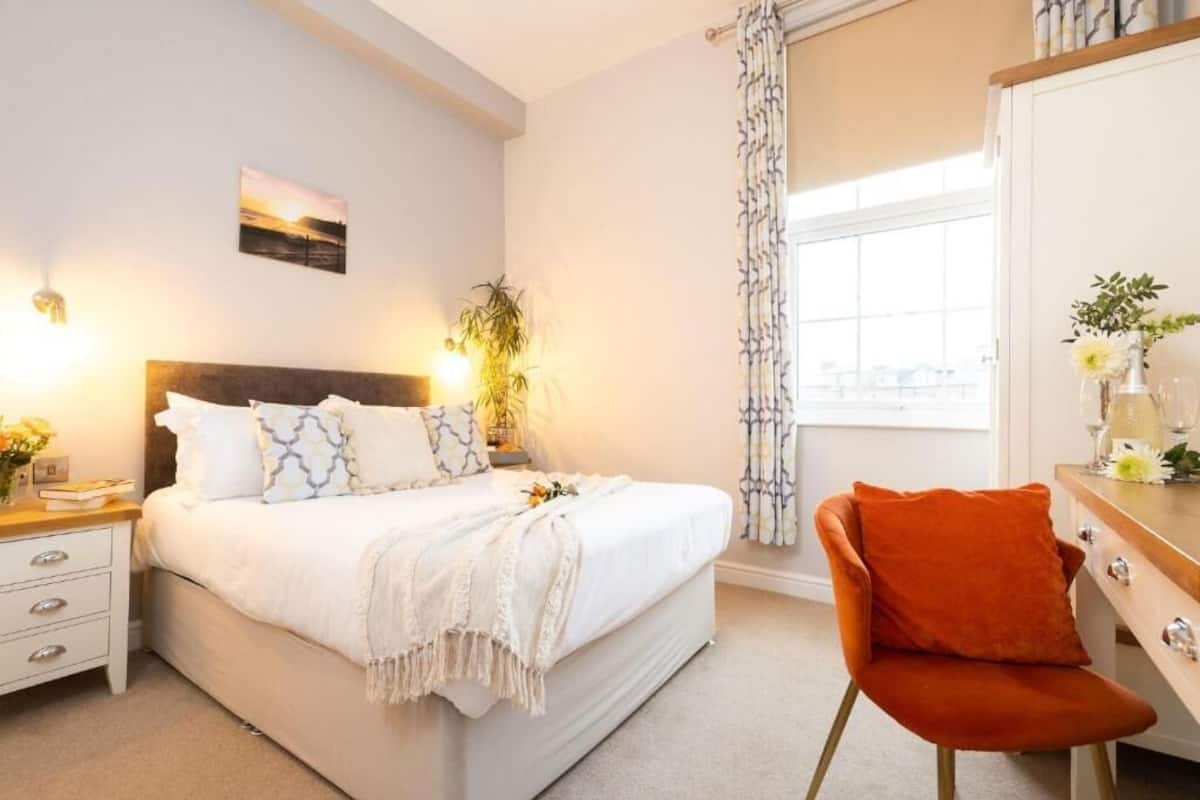 A bedroom with a bed, bedside table, chair, and a window with curtains.