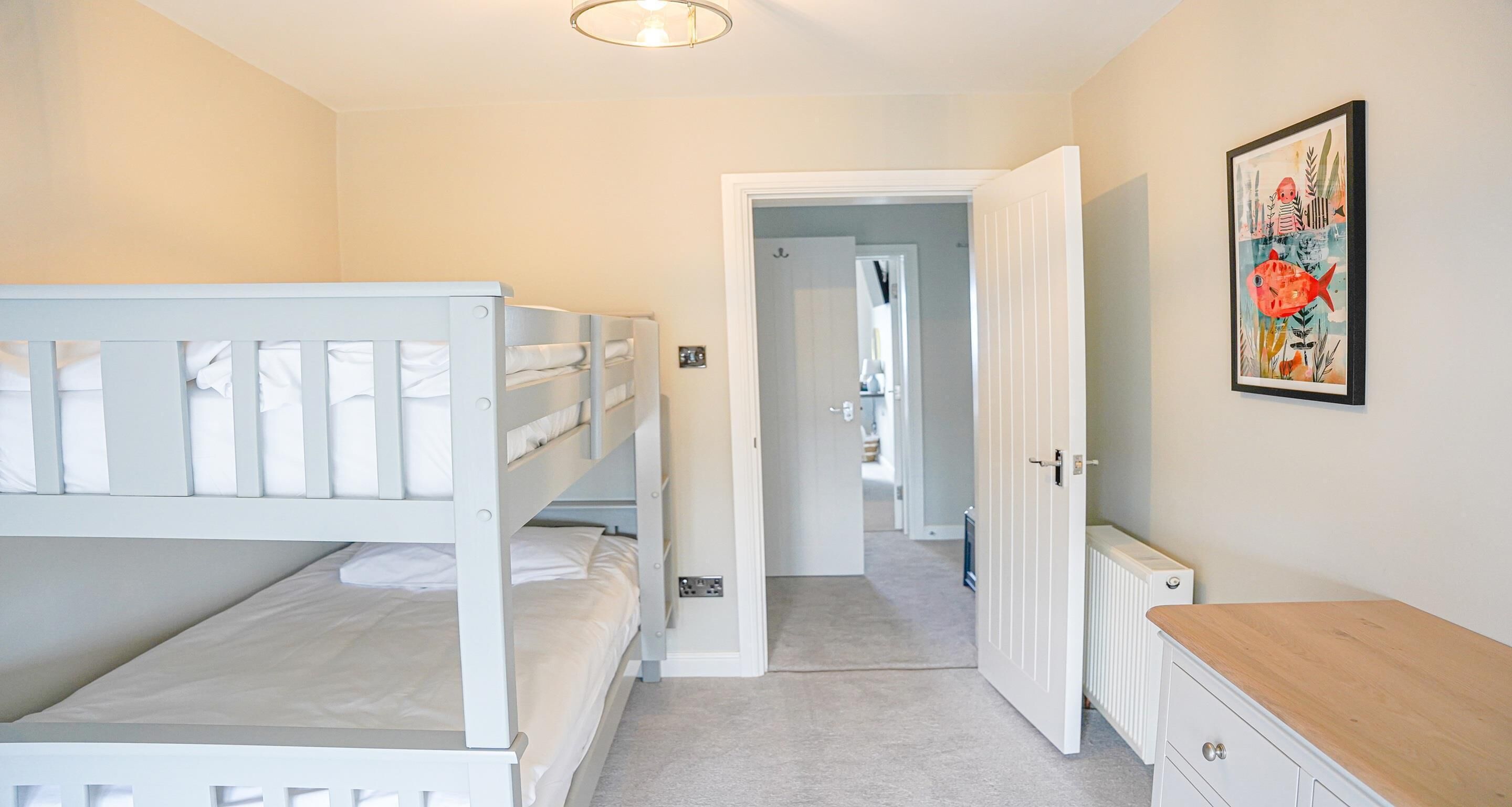 A bedroom with bunk beds, a door leading to another room, a radiator, and a framed picture on the wall.
