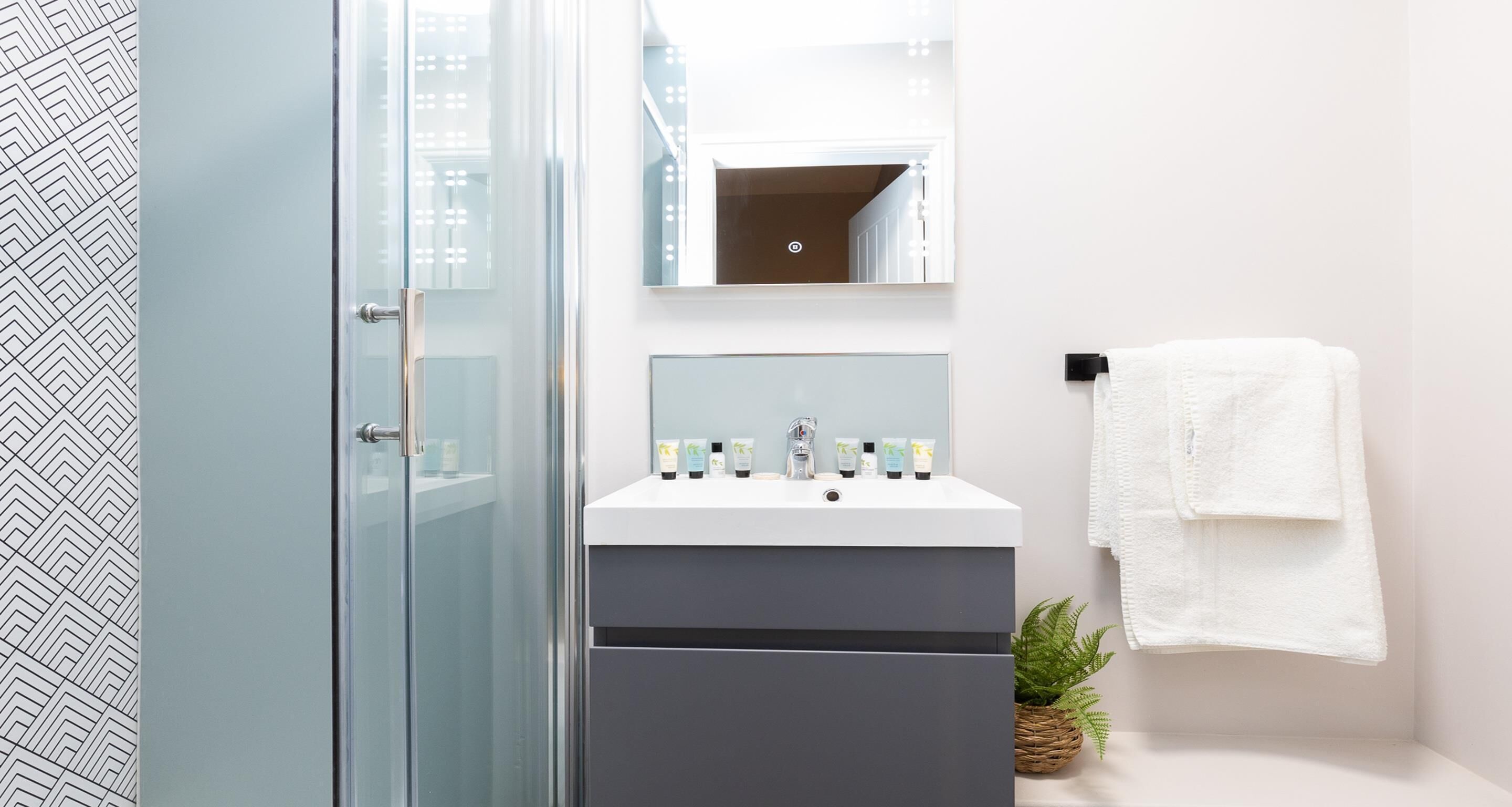Een moderne badkamer met een glazen douchecabine, een wit wastafelmeubel met toiletartikelen, en een witte handdoek aan een rek.