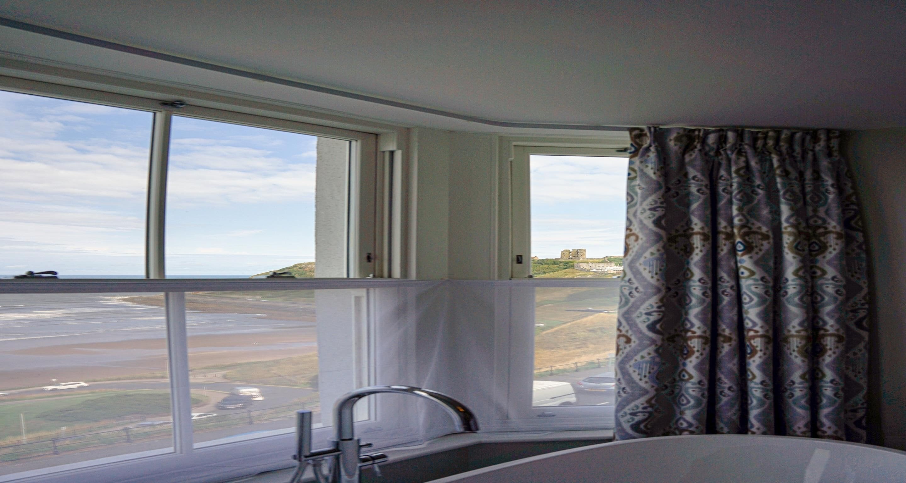 A bathroom with a large window, a bathtub, and a view of a coastal landscape.