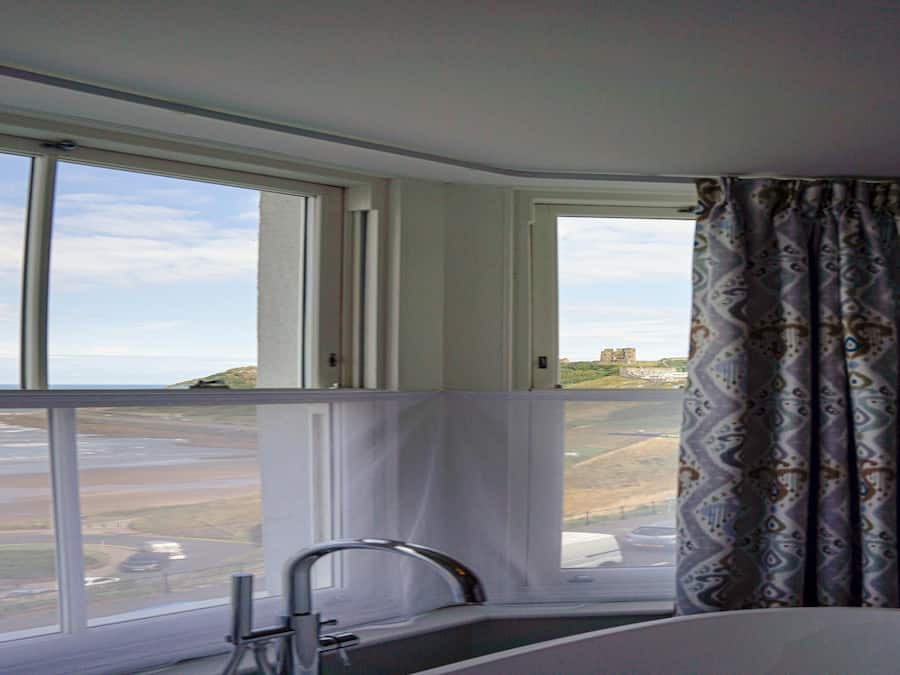 A bathroom with a large window, a bathtub, and a view of a coastal landscape.