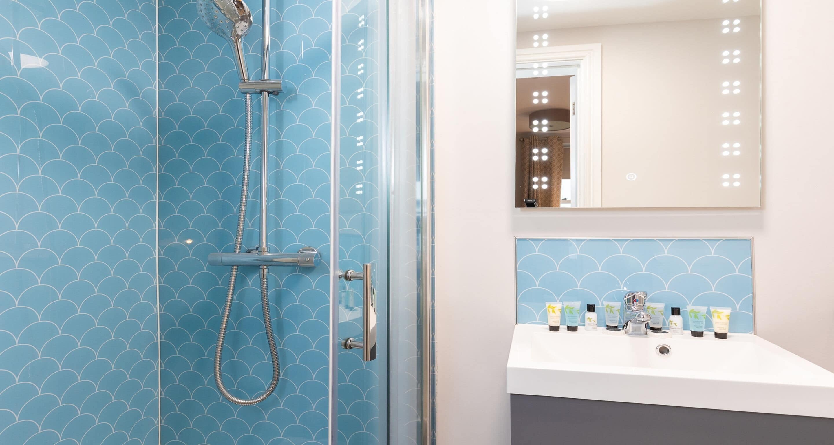 Ein Badezimmer mit blauen Fliesen, einer Glasdusche und einem weißen Waschbecken mit Toilettenartikeln.