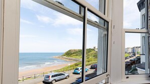 A coastal view from a window overlooking a beach, a road with cars, and a hilly landscape. - The Clarence Gardens Hotel, BW Signature Collection (Scarborough)