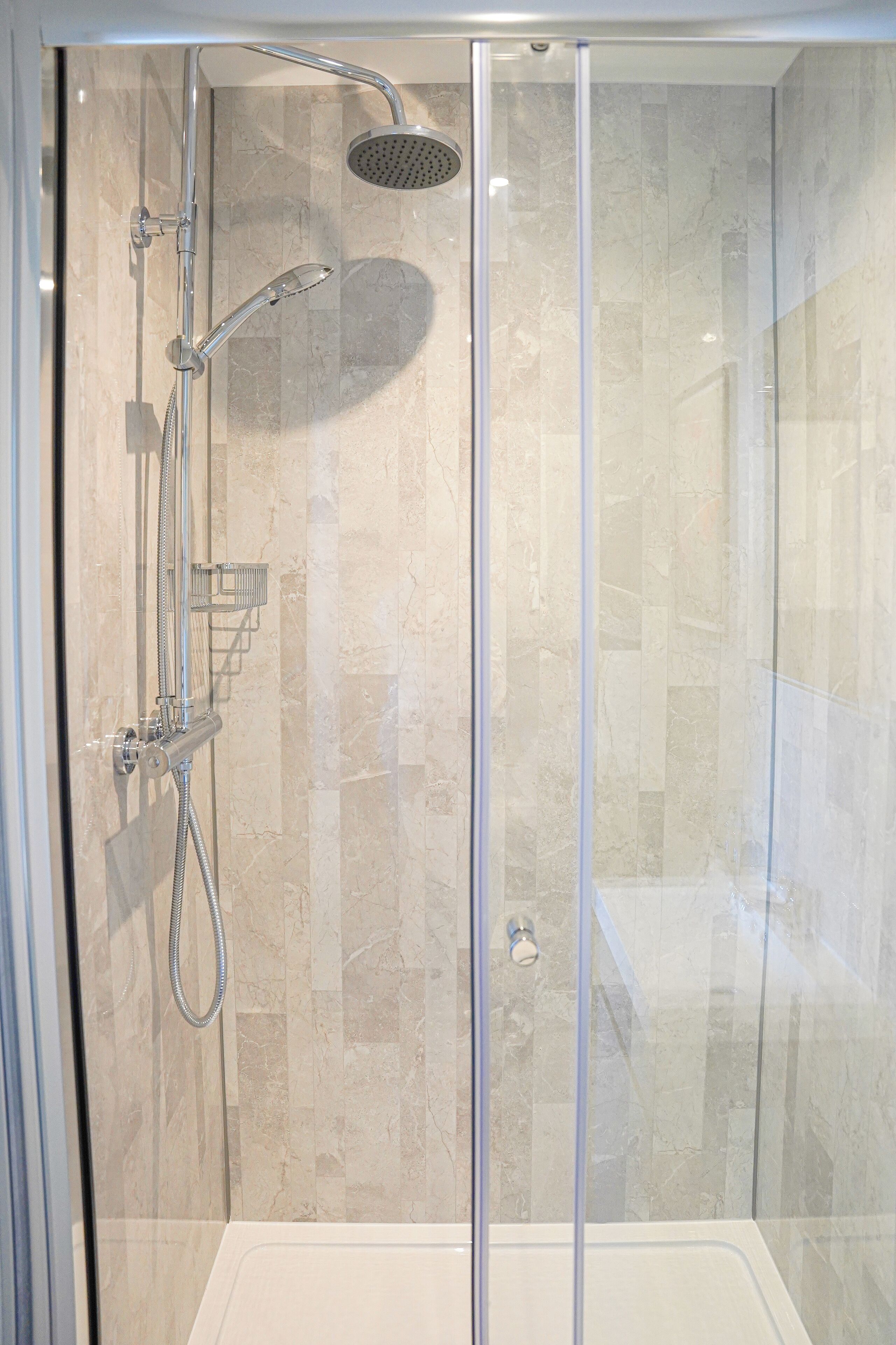 A glass-enclosed walk-in shower with a handheld showerhead, a wall-mounted faucet, and a control panel.