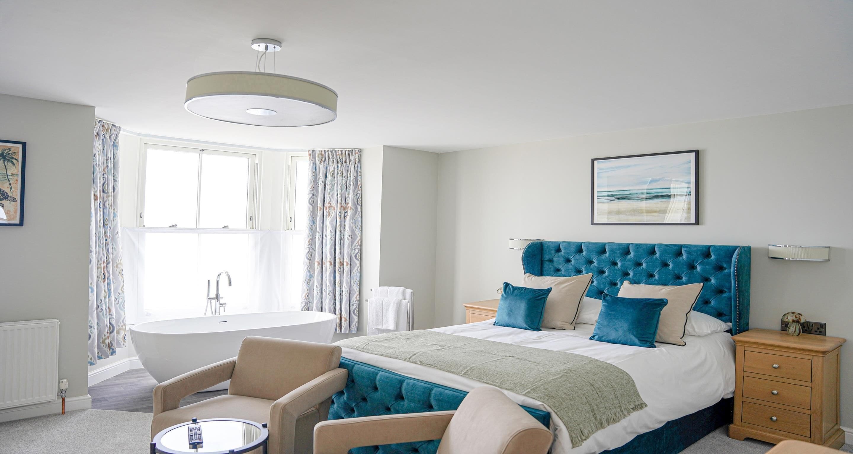 A bedroom with a large bed, a sitting area with a round table, a bathtub, and a window with curtains.
