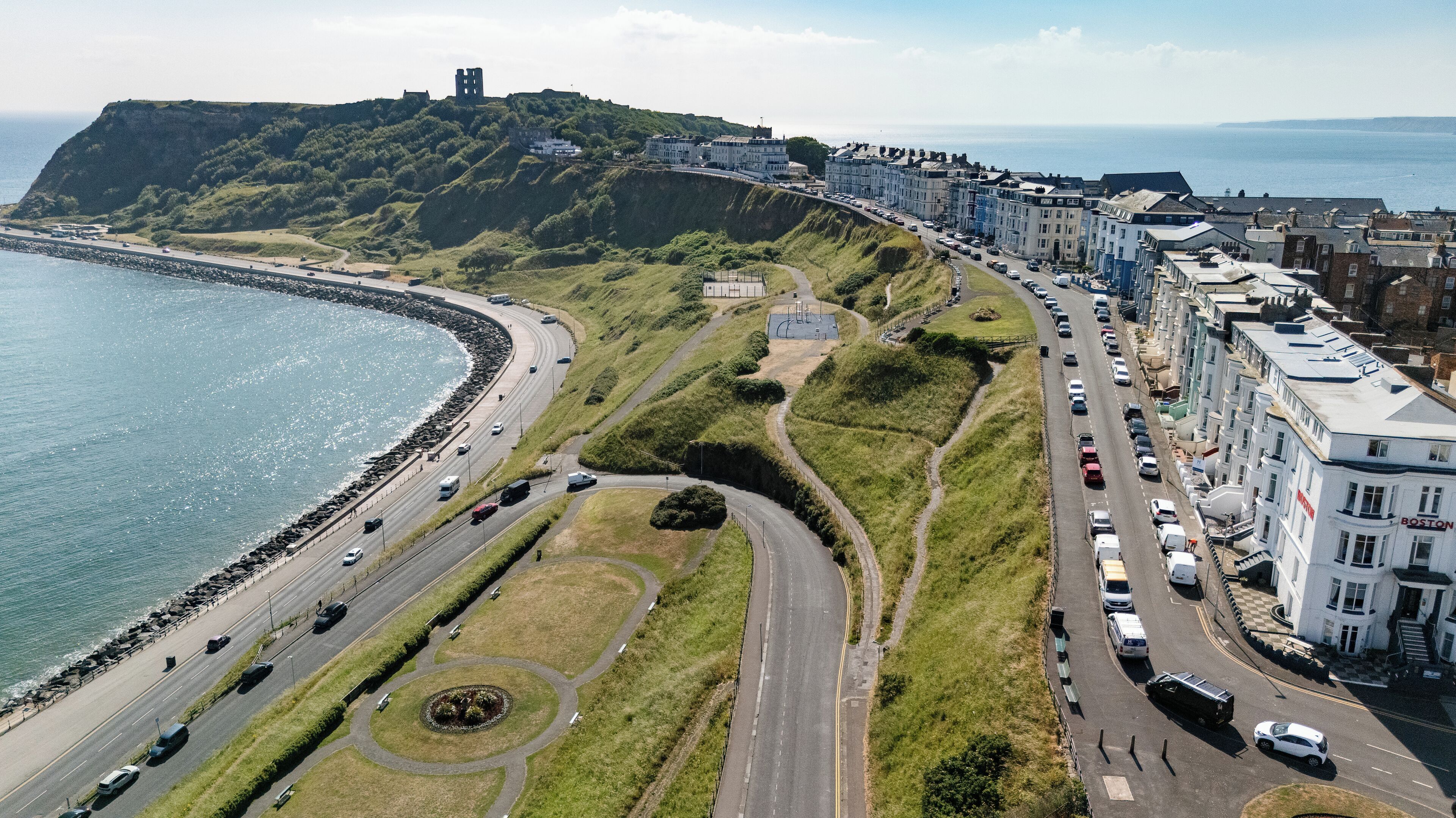 A coastal road with a beach on one side and a row of buildings on the other.