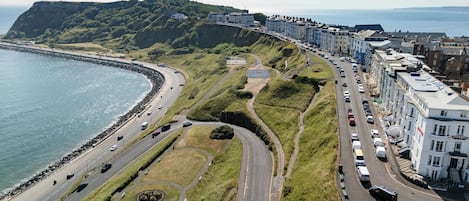 A coastal road with a beach on one side and a row of buildings on the other.