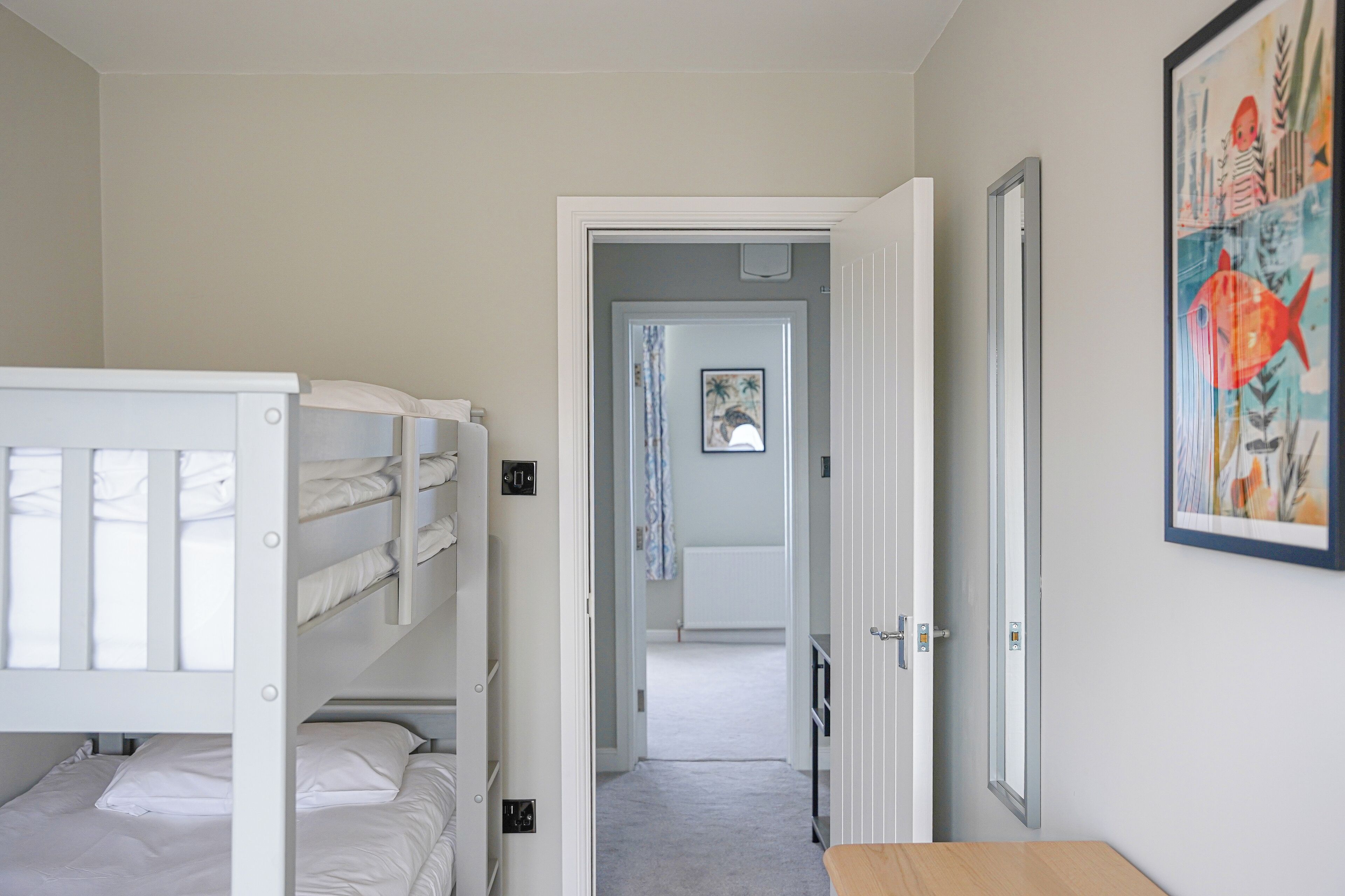 A bedroom with bunk beds, a door leading to another room, and a framed picture on the wall.