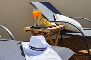A sun lounger with a dining table beside it, a white hat, and a glass of orange juice.