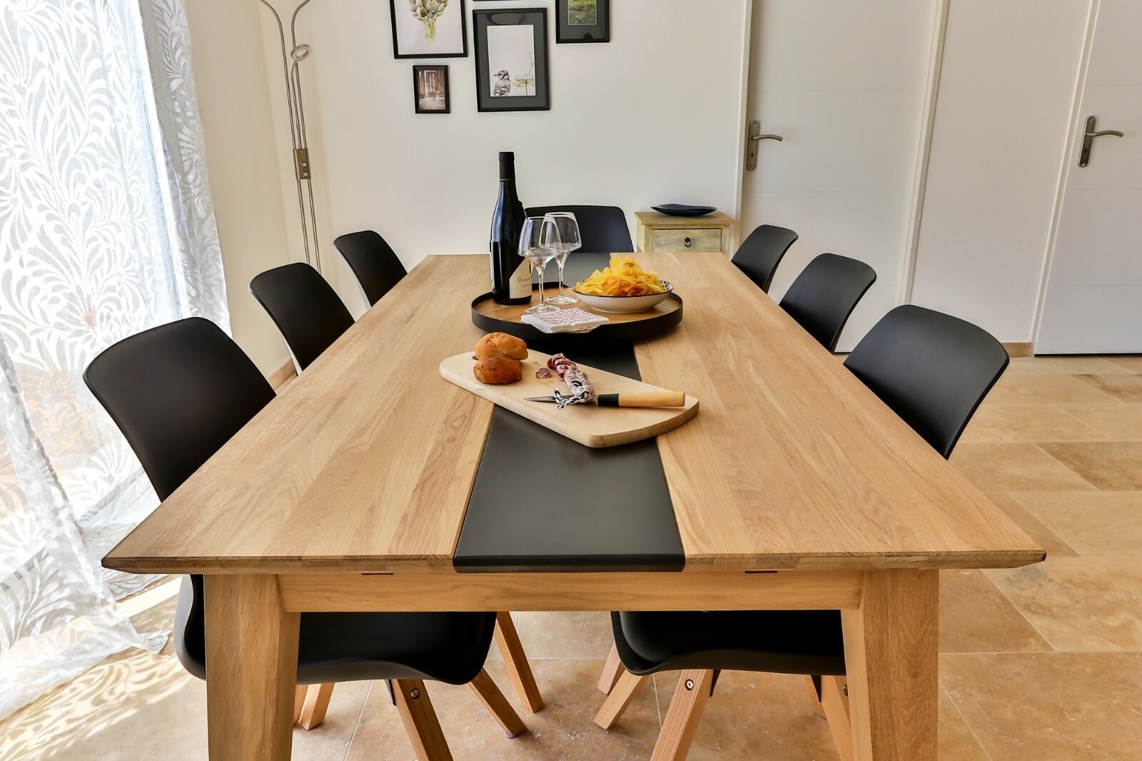 Une table à manger avec des chaises noires, une bouteille de vin et un saladier de fruits.