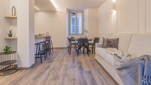 A modern living room with a sofa, a dining table with chairs, and a kitchen area with stools. - Casa Lenora in Bellano (Bellano)