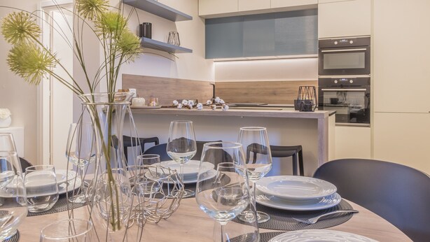 A modern kitchen with built-in appliances, a dining area with a table set for six, and a decorative vase with greenery. - Casa Lenora in Bellano (Bellano)