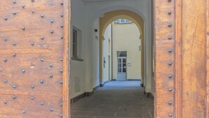 A hallway with a wooden door featuring metal studs, leading to a building with a tiled floor and an arched doorway. - Casa Lenora in Bellano (Bellano)