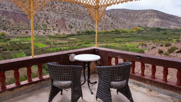 Una terraza con dos sillas de mimbre y una pequeña mesa, con vistas a un paisaje montañoso.