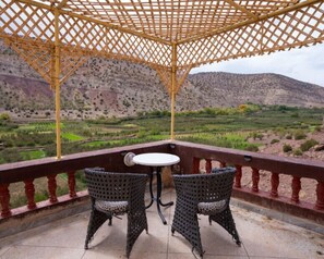A terrace with two wicker chairs and a small table, overlooking a mountainous landscape.