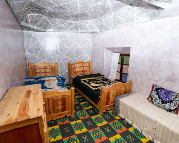 A small, cozy room with two wooden beds, a small table, and a colorful patterned floor.