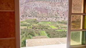 Una habitación con un amplio ventanal que ofrece vistas a un paisaje montañoso con campos en terrazas y vegetación escasa.