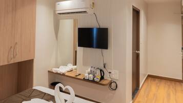 A hotel room with a bed, a ceiling fan, an air conditioning unit, a flat-screen TV, and a small table with toiletries.