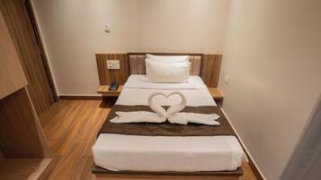 A hotel room with a wooden bed, a heart-shaped towel arrangement, a bedside table, and a nightstand.