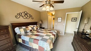 A bedroom with a large bed, a dresser, a ceiling fan, and a door leading to another room. - Hot Springs Village Condo on the Green (Hot Springs)