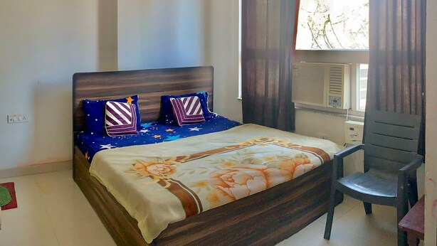 Een slaapkamer met een bed, een stoel, een plafondventilator en een raam met gordijnen.
