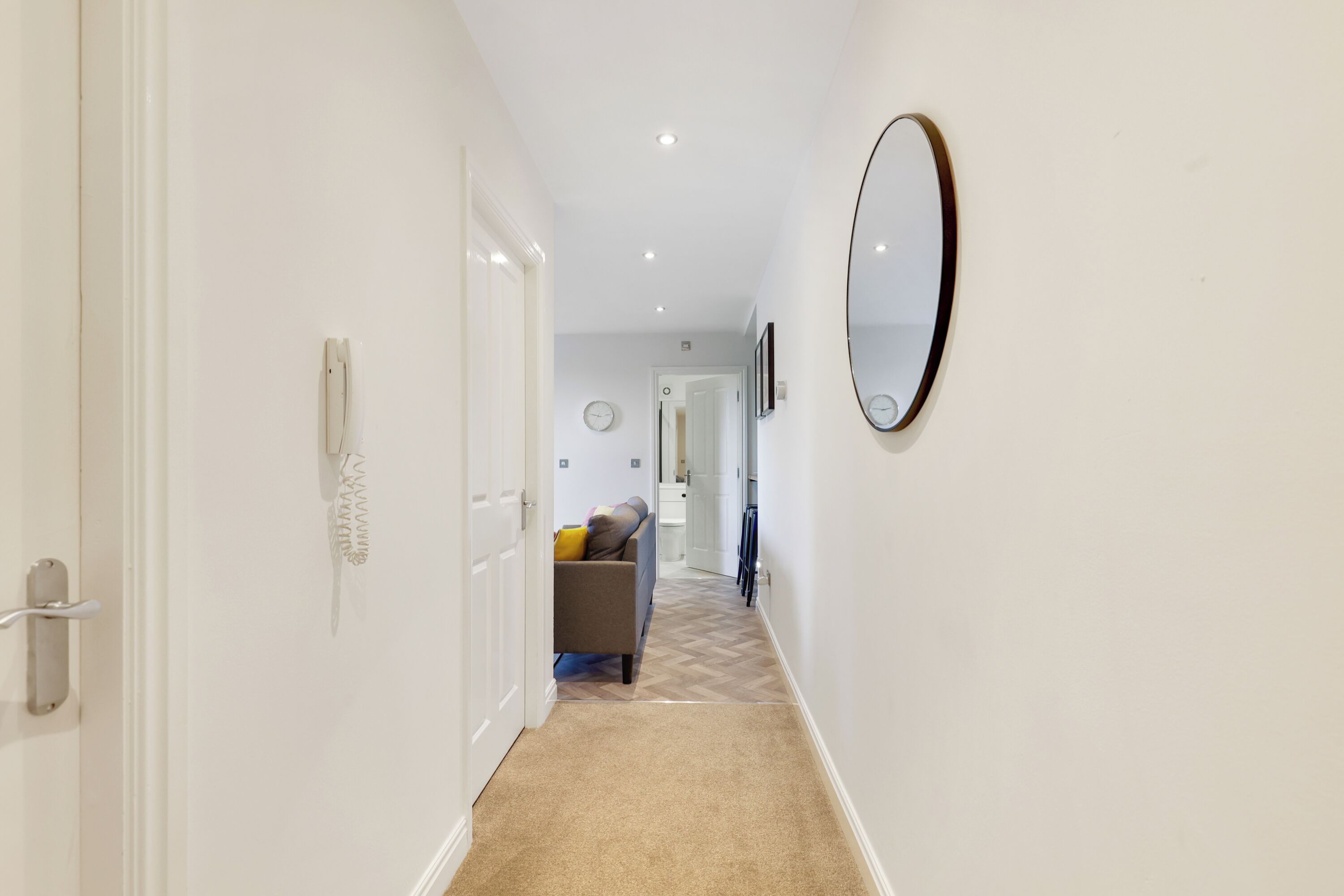 Un couloir avec un sol recouvert de moquette, un canapé, un miroir et une porte.