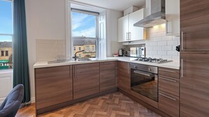 A modern kitchen with wooden cabinets, a built-in oven, and a window with a view of buildings. - Darjeeling - North East Escapes (Alnwick)