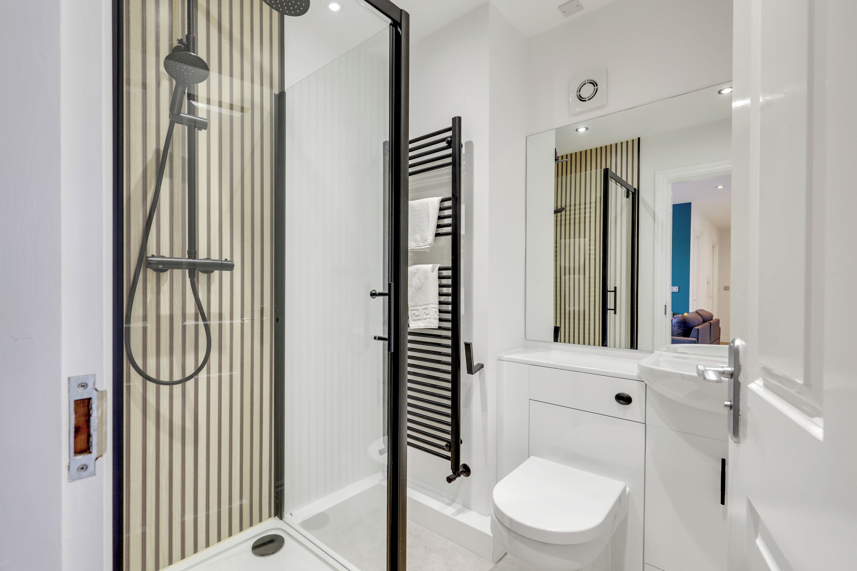 Un baño moderno con cabina de ducha de vidrio, inodoro blanco y toallero negro.