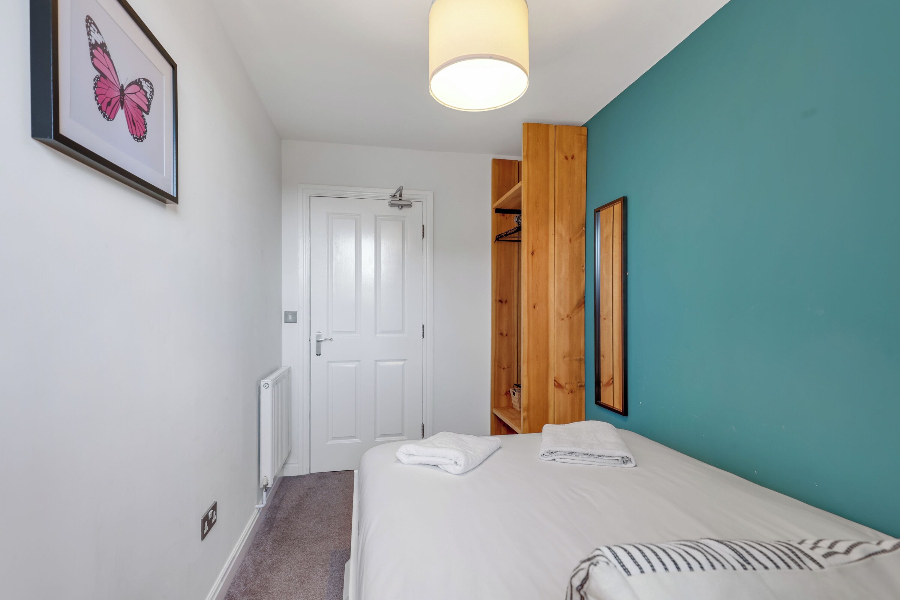 Un dormitorio con cama, una puerta blanca, un armario de madera, un cuadro enmarco y una lámpara en el techo.