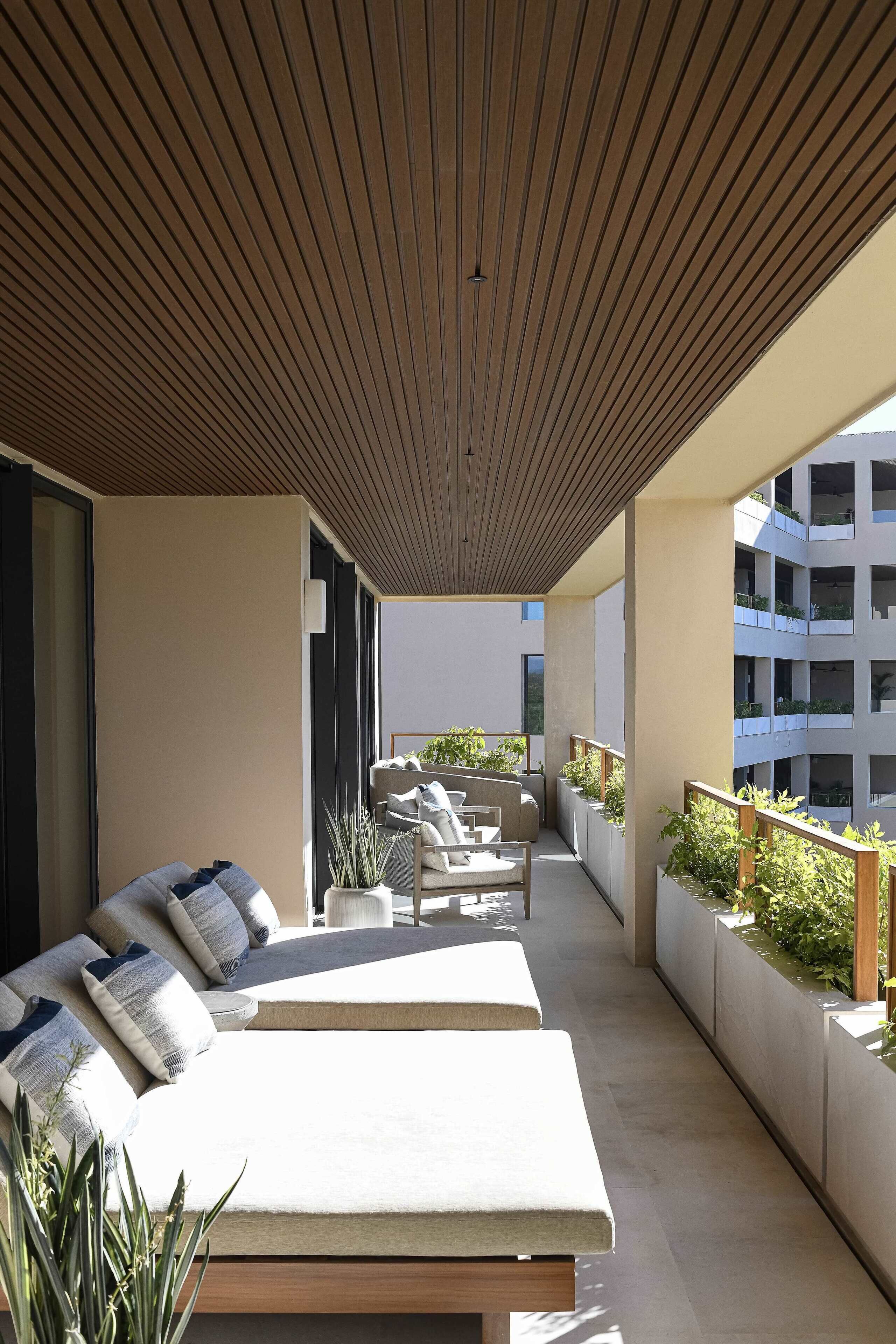 A modern outdoor lounge area with a wooden ceiling, cushioned seating, and planters.