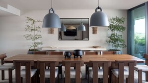 Zona pranzo moderna con tavolo e sedie in legno, luci a sospensione e piante in vaso.