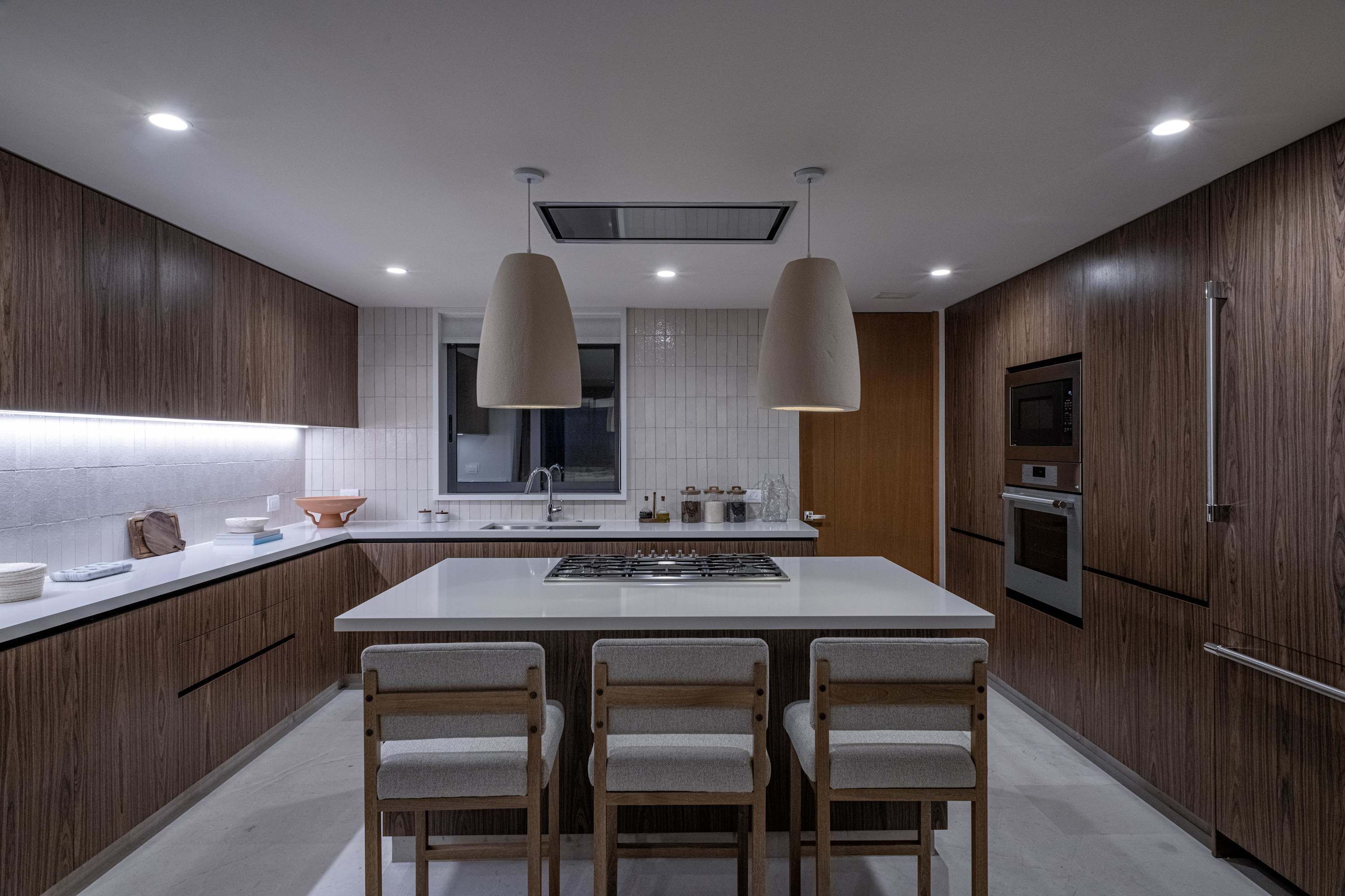 A modern kitchen with wooden cabinets, a central island with bar stools, a microwave, oven, and a refrigerator.
