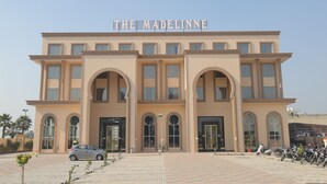 Un edificio con un cartello che riporta la scritta “THE MADELINNE” e un’area di parcheggio con diverse auto.