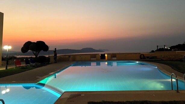 En swimmingpool med udsigt til solnedgang og bjerge i baggrunden.
