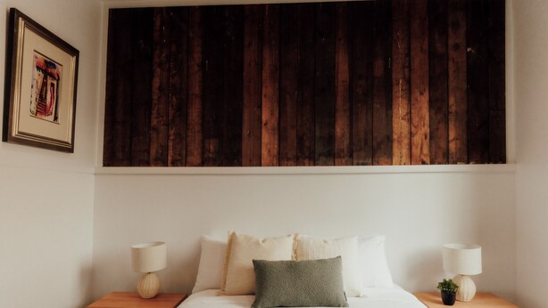 A bedroom with a wooden headboard, a bed with white bedding, two bedside tables with lamps, and a small potted plant.