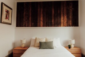 A bedroom with a wooden headboard, a bed with white bedding, two bedside tables with lamps, and a small potted plant. - Launceston Central Stay | Charming 2 Ensuites (Launceston City)