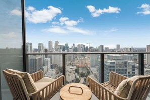 Ett rum högt upp i en skyskrapa med en fantastisk panoramautsikt över staden, två fåtöljer i rotting, ett litet runt bord och ett stort fönster.